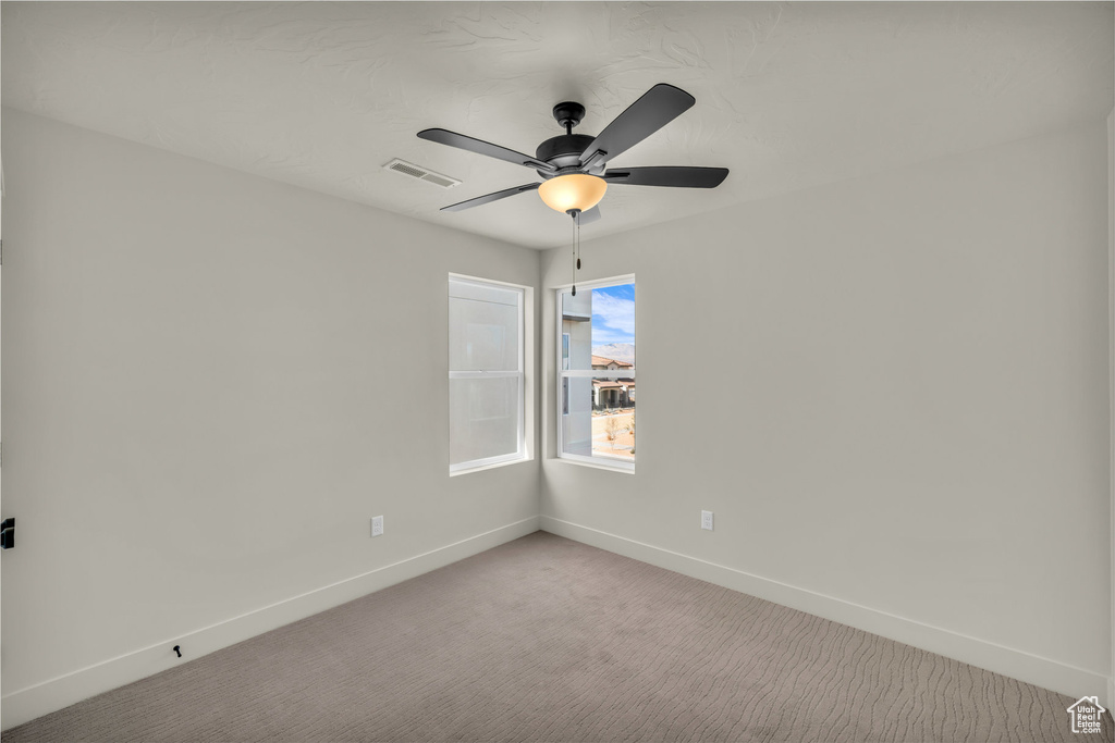 Spare room featuring light carpet, a ceiling fan, visible vents, and baseboards