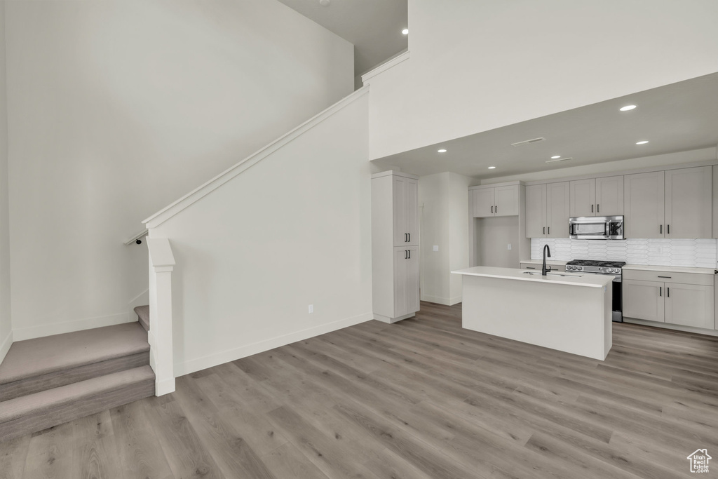 Kitchen with stainless steel appliances, decorative backsplash, light wood-style floors, an island with sink, and baseboards