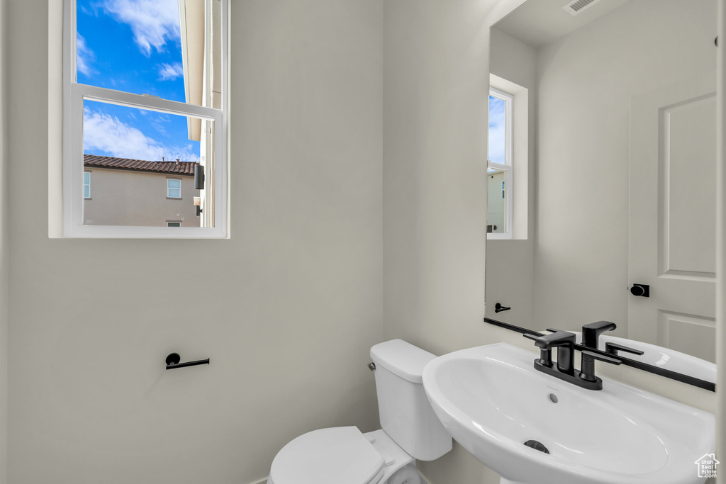 Half bath with toilet, a sink, and visible vents