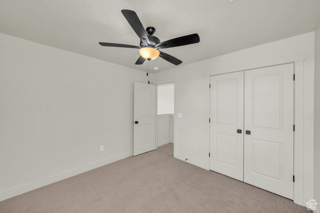 Unfurnished bedroom featuring a closet, light colored carpet, ceiling fan, and baseboards