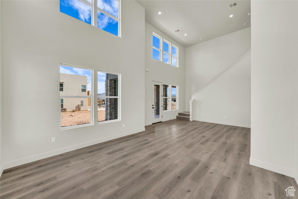 Unfurnished living room with stairs, wood finished floors, visible vents, and baseboards