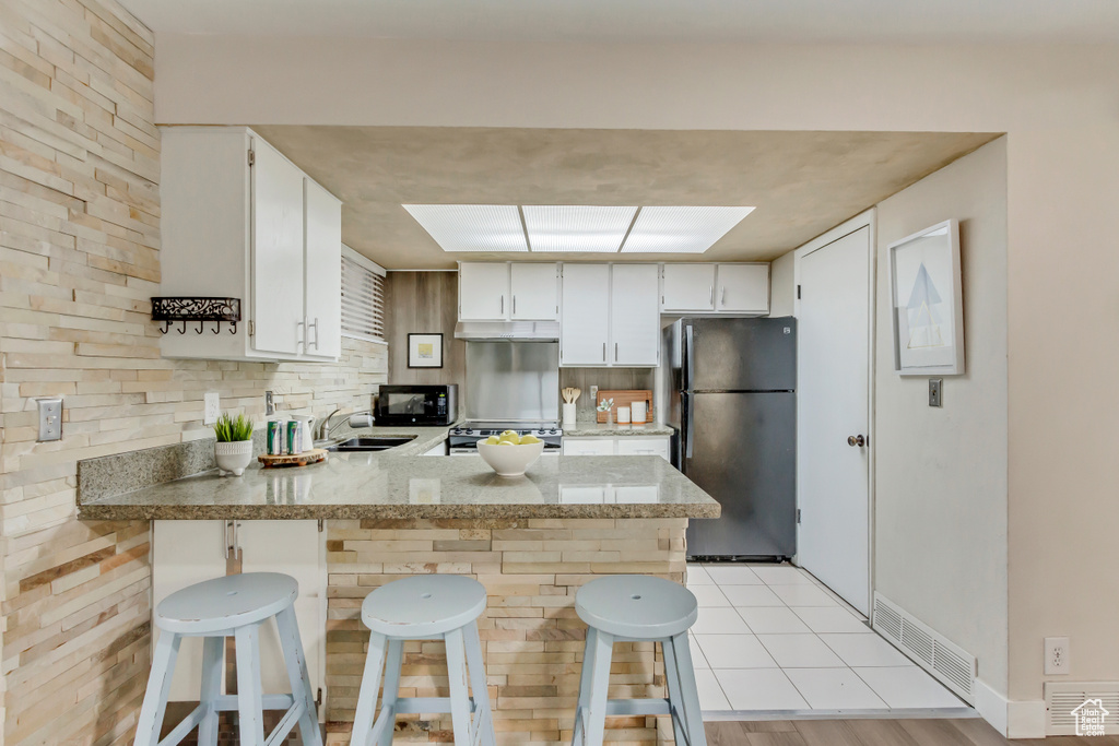 Kitchen with visible vents, a peninsula, under cabinet range hood, black appliances, and a sink