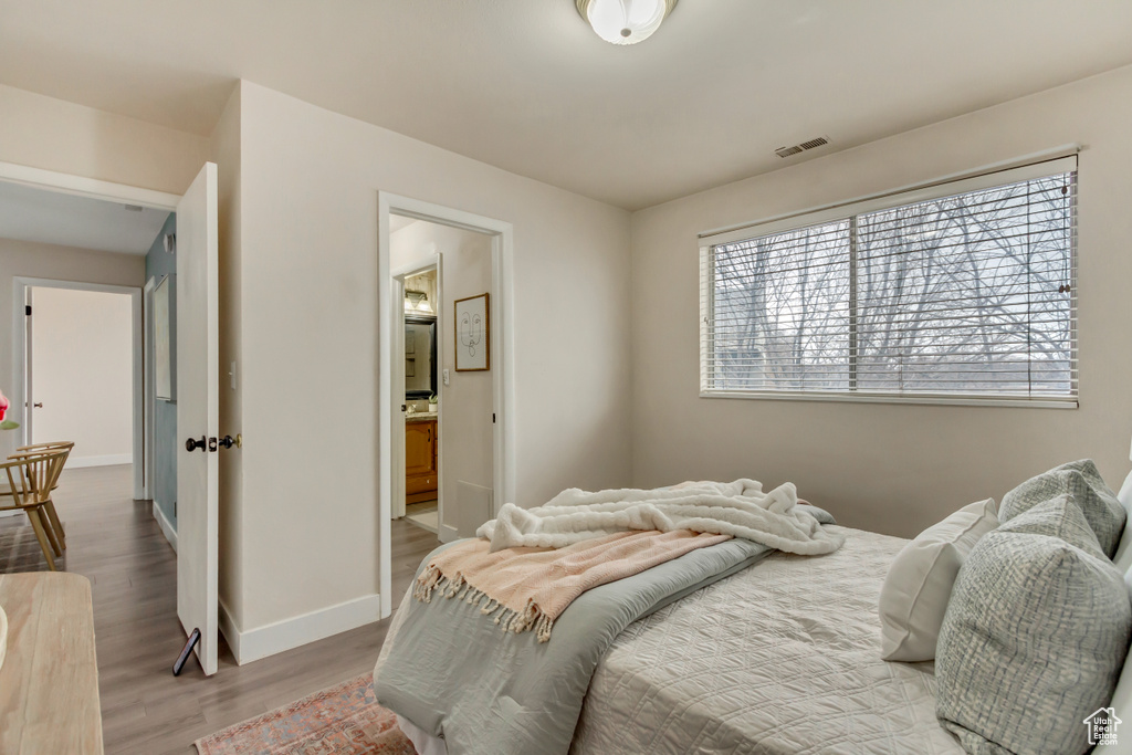 Bedroom with baseboards, connected bathroom, visible vents, and wood finished floors