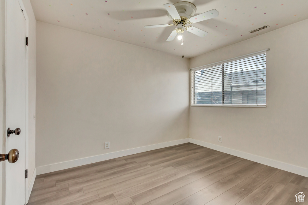 Empty room with light wood-style flooring, visible vents, ceiling fan, and baseboards