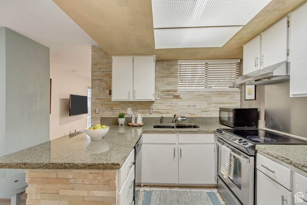 Kitchen featuring black microwave, under cabinet range hood, a peninsula, a sink, and electric stove