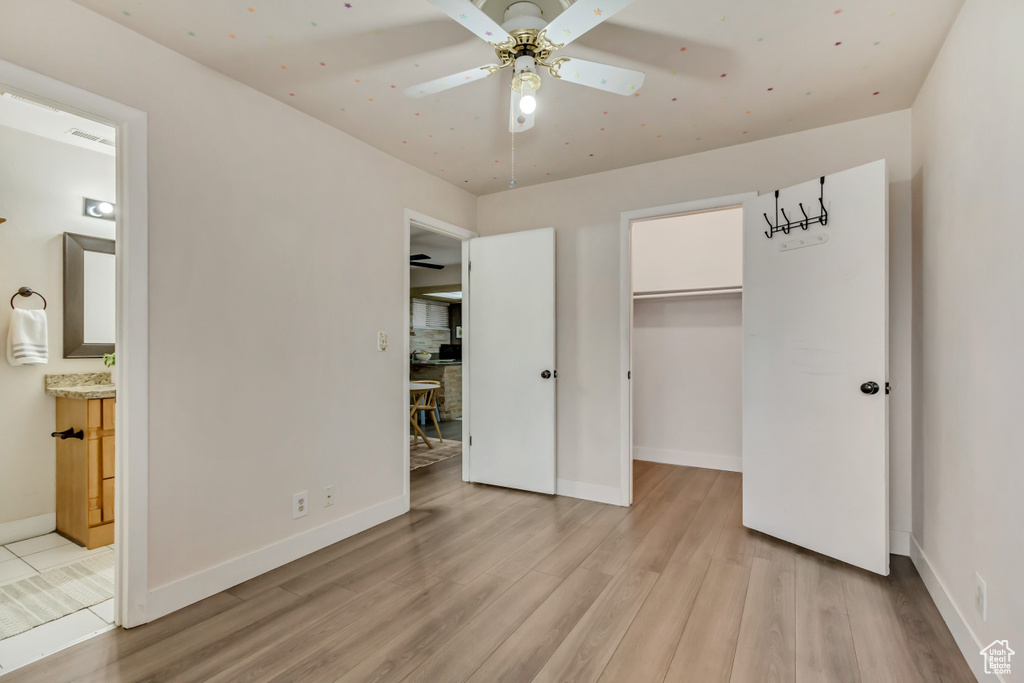 Unfurnished bedroom featuring light wood-type flooring, a walk in closet, connected bathroom, and baseboards