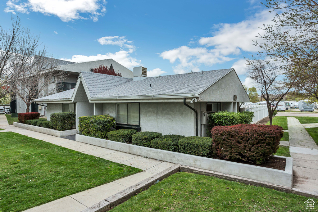 View of side of property with stucco siding, roof with shingles, a chimney, and a yard