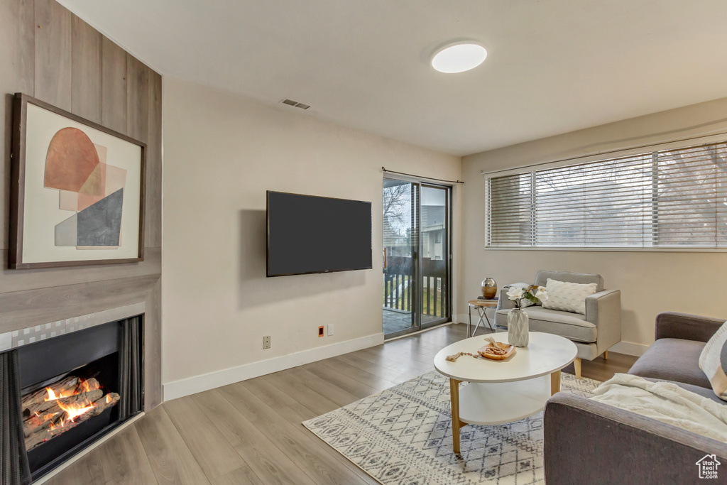 Living area featuring light wood-style floors, a warm lit fireplace, visible vents, and baseboards