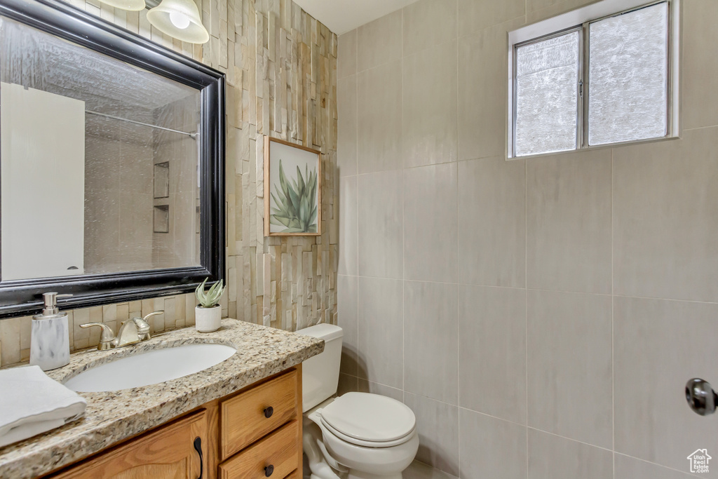 Bathroom featuring toilet, a shower, vanity, and tile walls