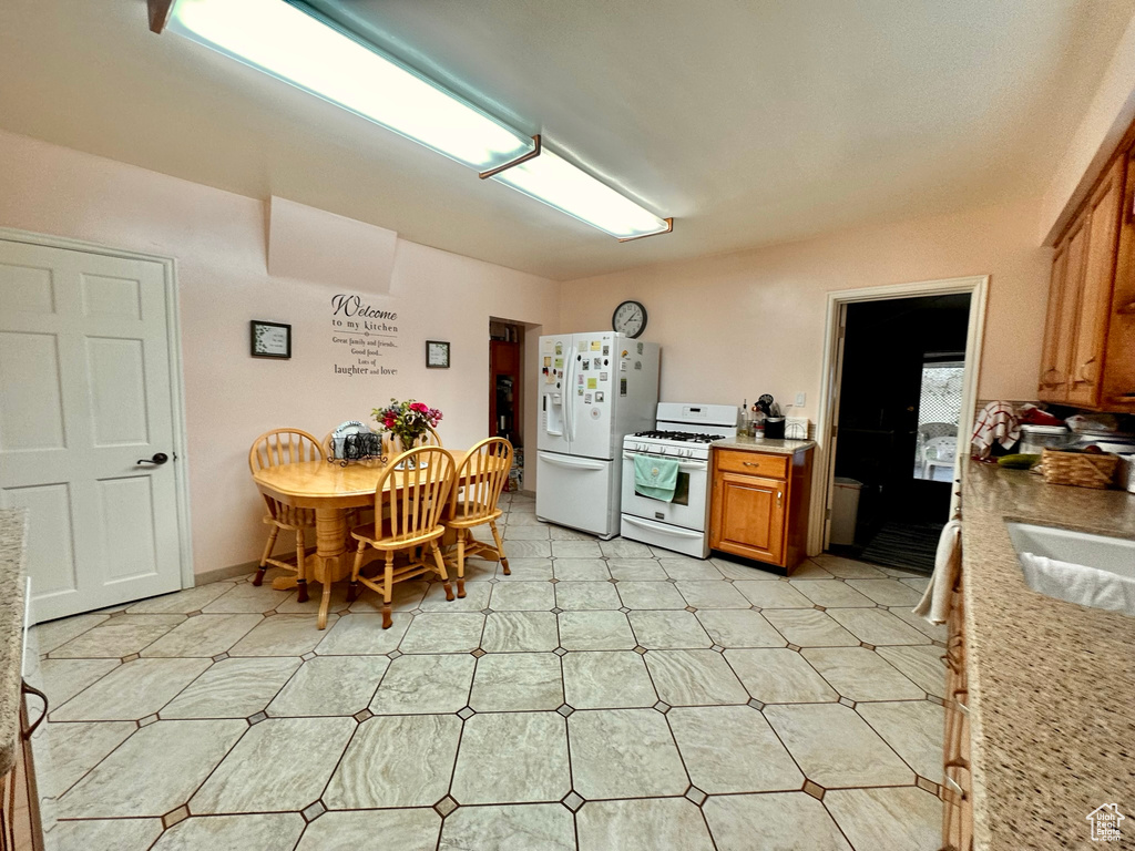 Kitchen featuring white appliances, brown cabinets, light countertops, light floors, and a sink