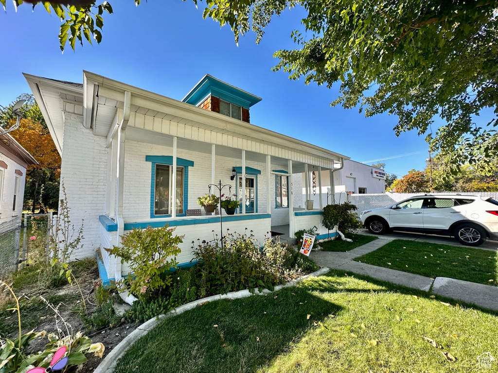 View of front of property featuring covered porch, a front yard, fence, and brick siding