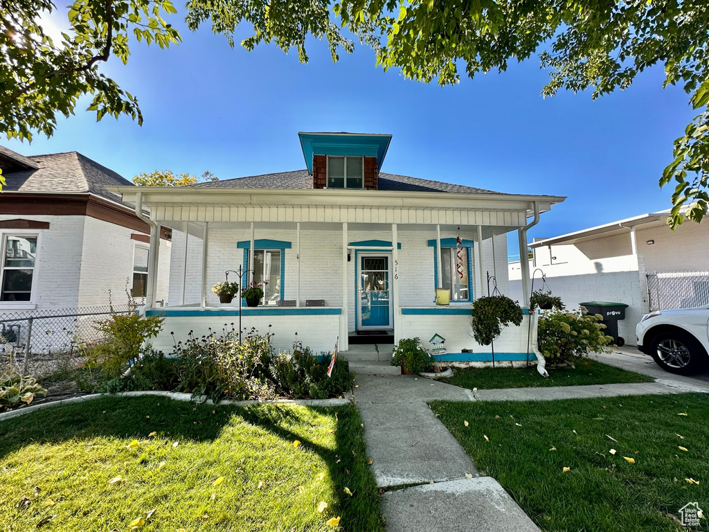 Bungalow-style home with a front lawn, fence, a porch, and brick siding