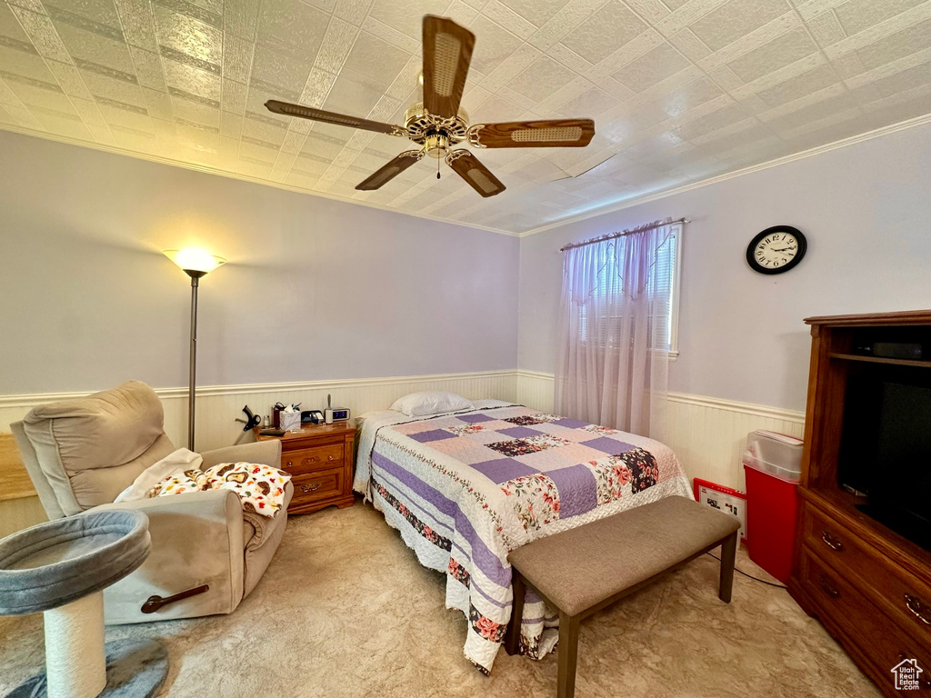 Bedroom with a ceiling fan, wainscoting, crown molding, and light carpet