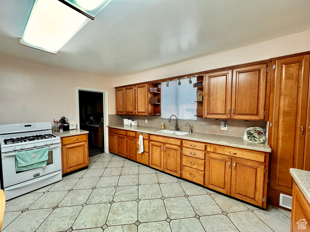 Kitchen with white gas stove, a sink, brown cabinets, decorative backsplash, and open shelves