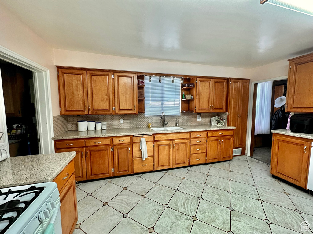 Kitchen featuring open shelves, tasteful backsplash, brown cabinets, and a sink
