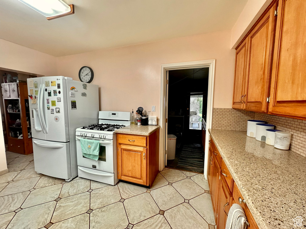 Kitchen with white appliances, light stone counters, brown cabinetry, and decorative backsplash