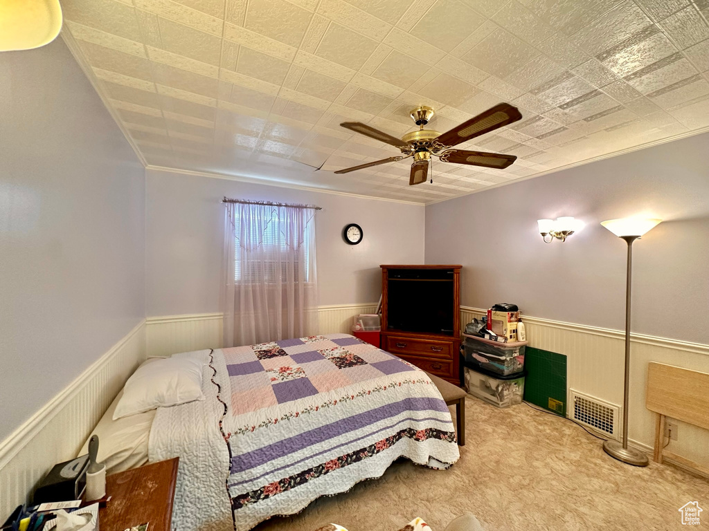 Carpeted bedroom featuring a wainscoted wall, visible vents, and a ceiling fan