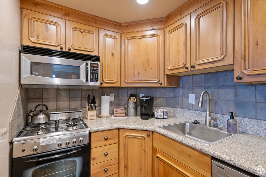 Kitchen with appliances with stainless steel finishes, backsplash, a sink, and light countertops