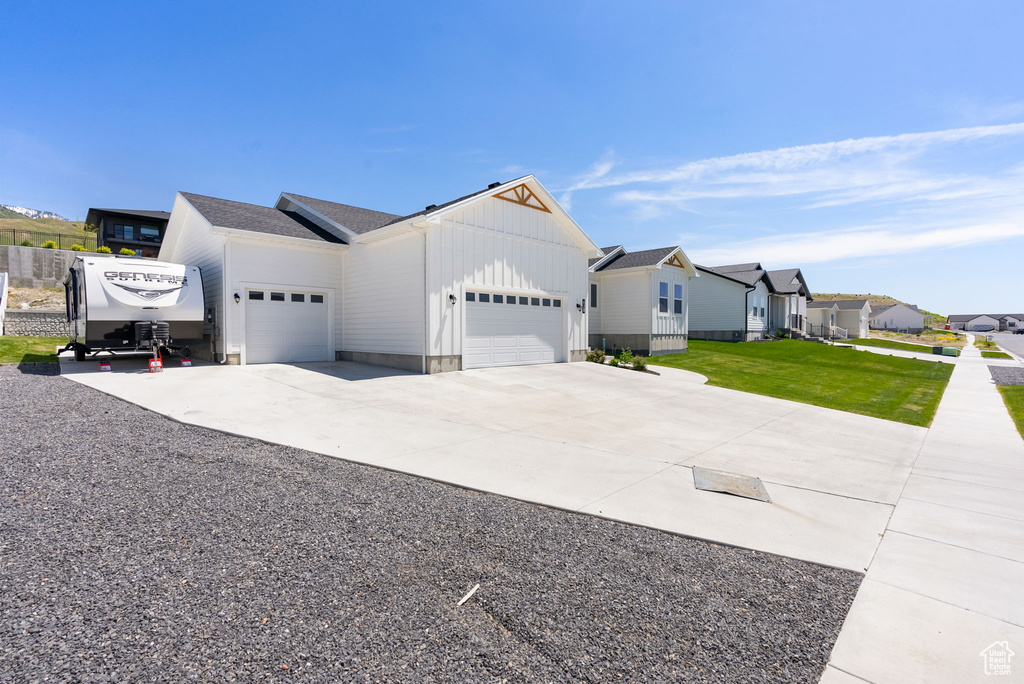 View of front facade with a garage, board and batten siding, concrete driveway, a residential view, and a front lawn