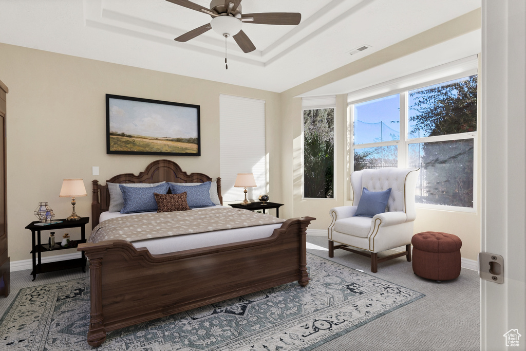 Carpeted bedroom featuring a tray ceiling, a ceiling fan, visible vents, and baseboards