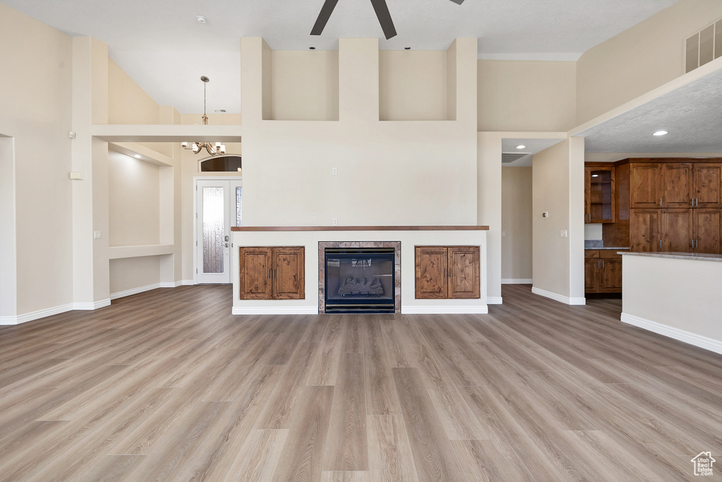 Unfurnished living room featuring high vaulted ceiling, light wood finished floors, a fireplace, and visible vents