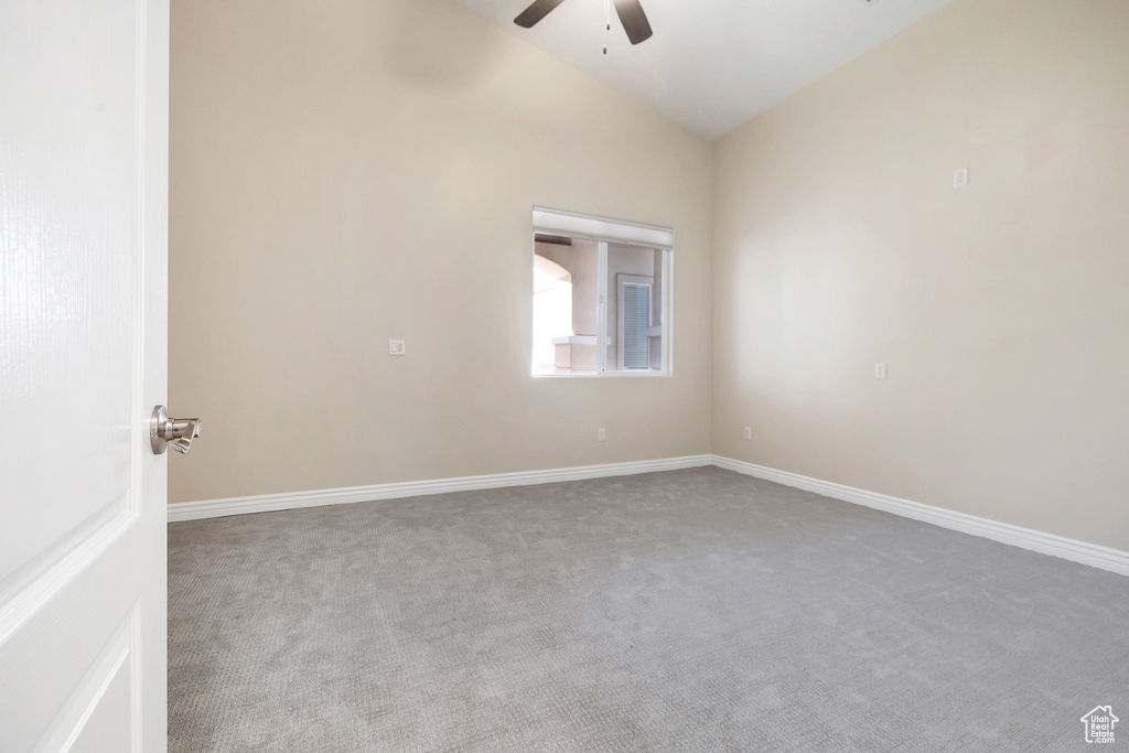 Carpeted spare room featuring baseboards, vaulted ceiling, and a ceiling fan