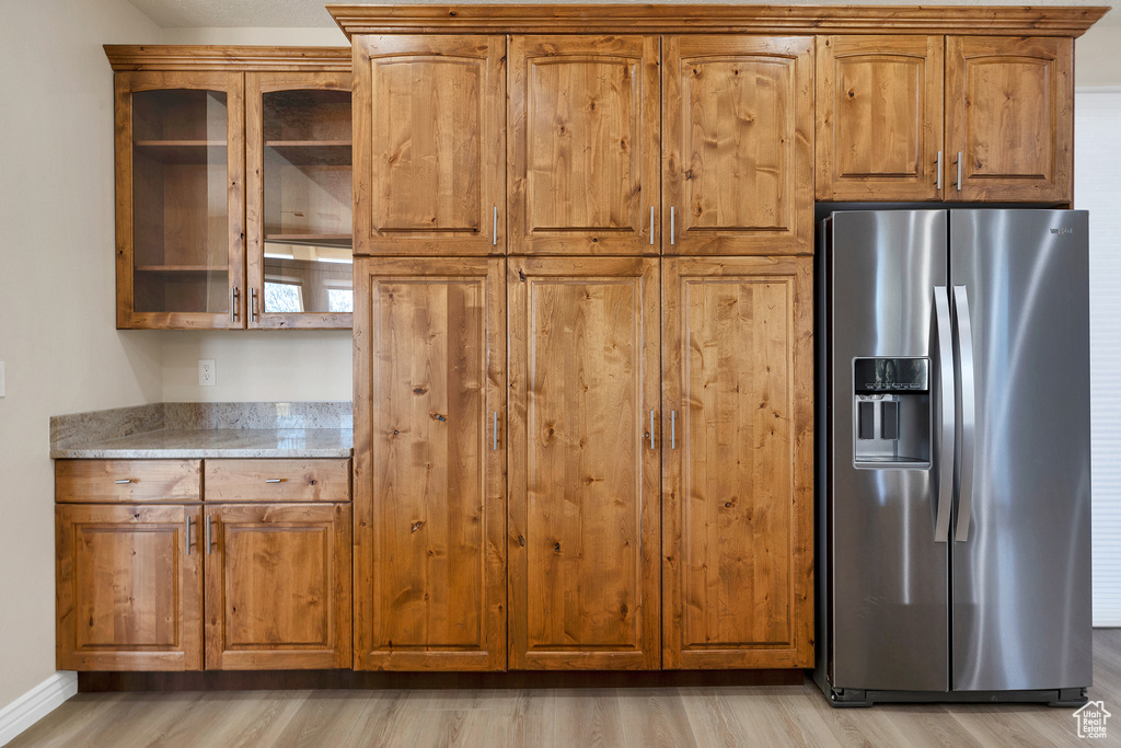 Kitchen featuring brown cabinets, light wood-style flooring, stainless steel fridge with ice dispenser, and light stone countertops