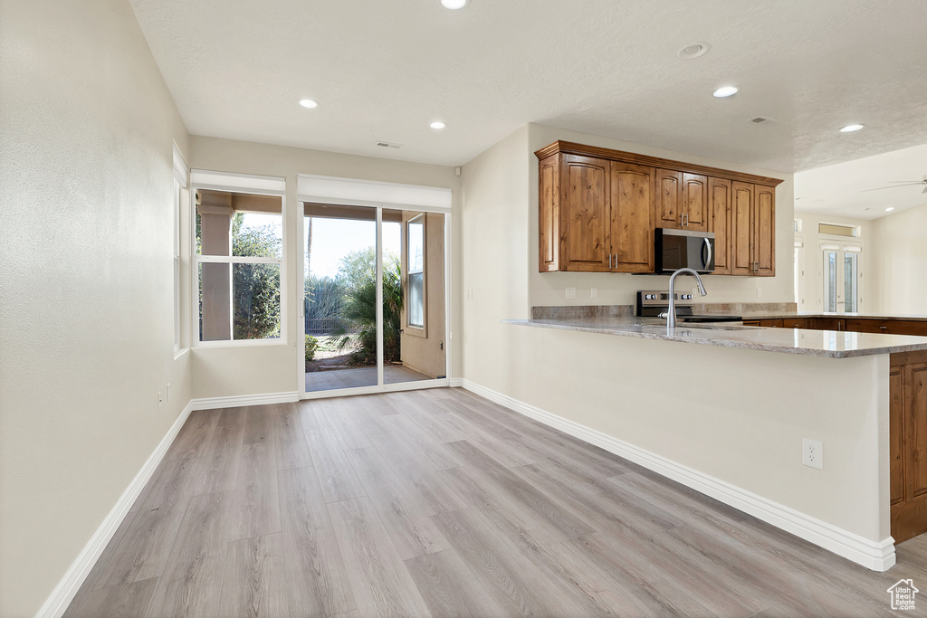 Kitchen featuring a peninsula, baseboards, light wood-style floors, appliances with stainless steel finishes, and brown cabinets
