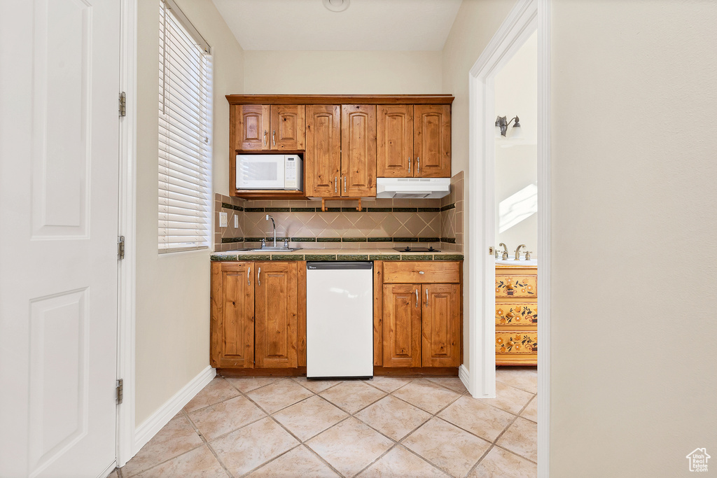 Kitchen featuring white appliances, tile counters, decorative backsplash, under cabinet range hood, and a sink
