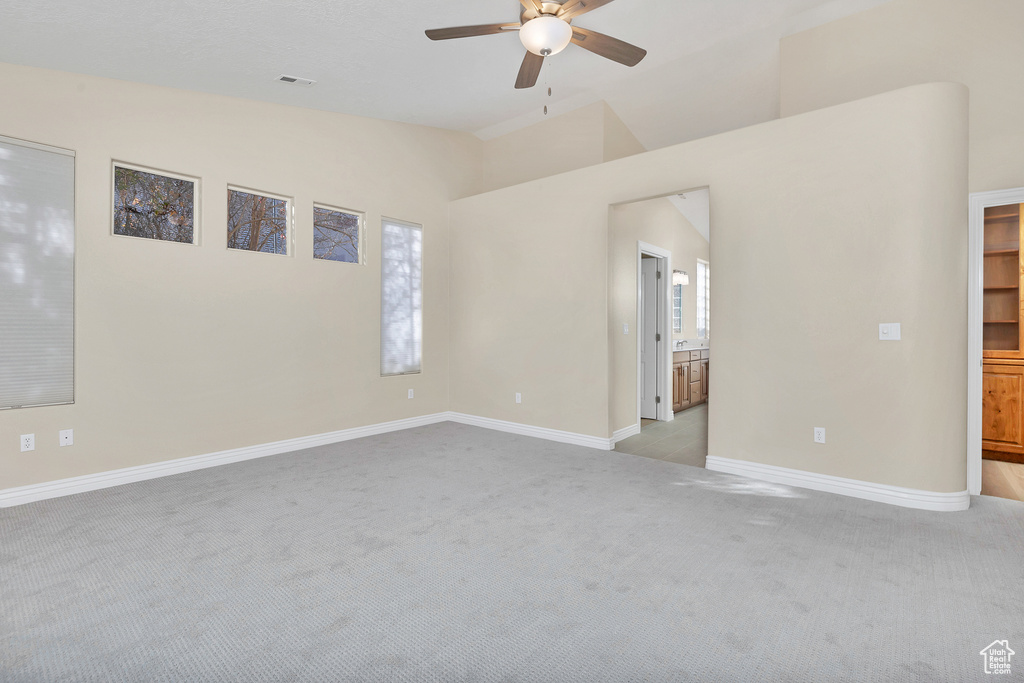 Empty room with lofted ceiling, ceiling fan, baseboards, and light colored carpet