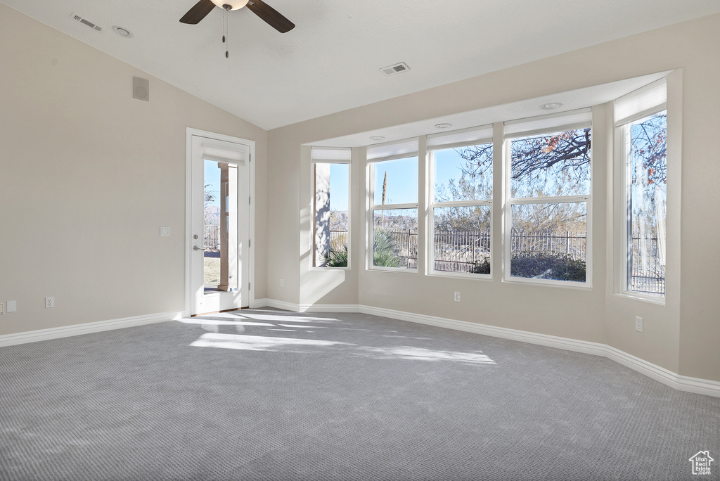 Carpeted spare room with lofted ceiling, a ceiling fan, visible vents, and baseboards