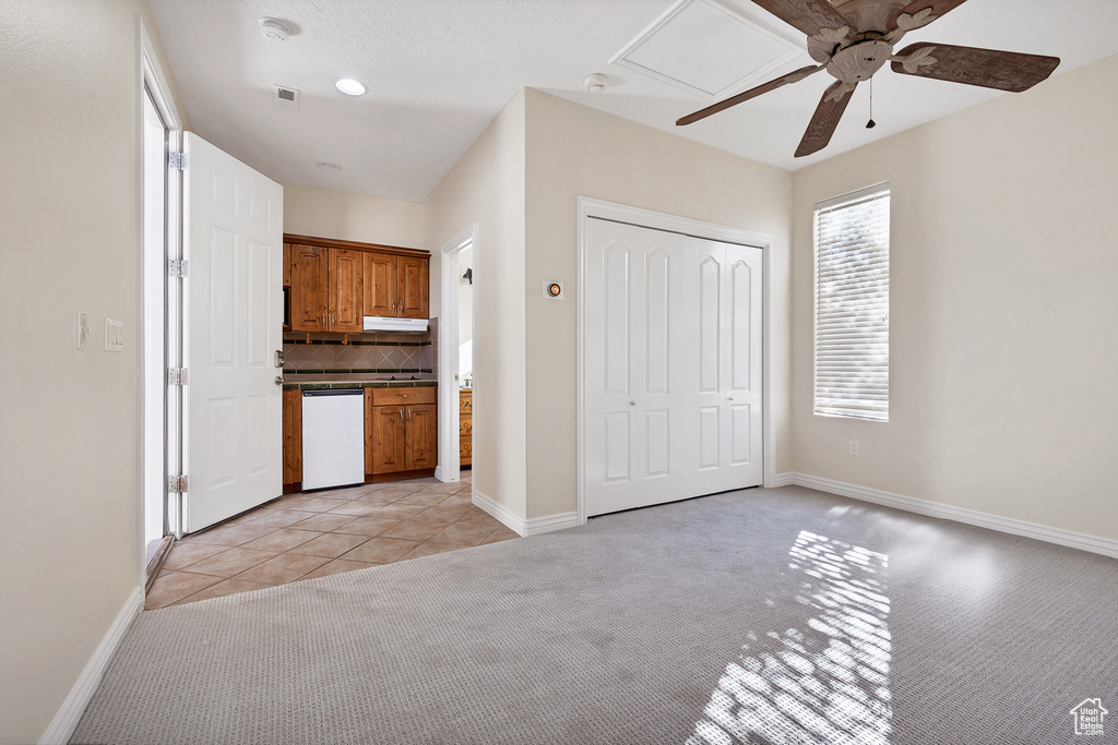 Kitchen with brown cabinets, tasteful backsplash, dark countertops, light colored carpet, and dishwasher