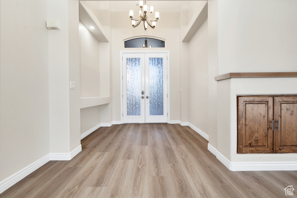 Foyer with light wood finished floors, french doors, a chandelier, and baseboards