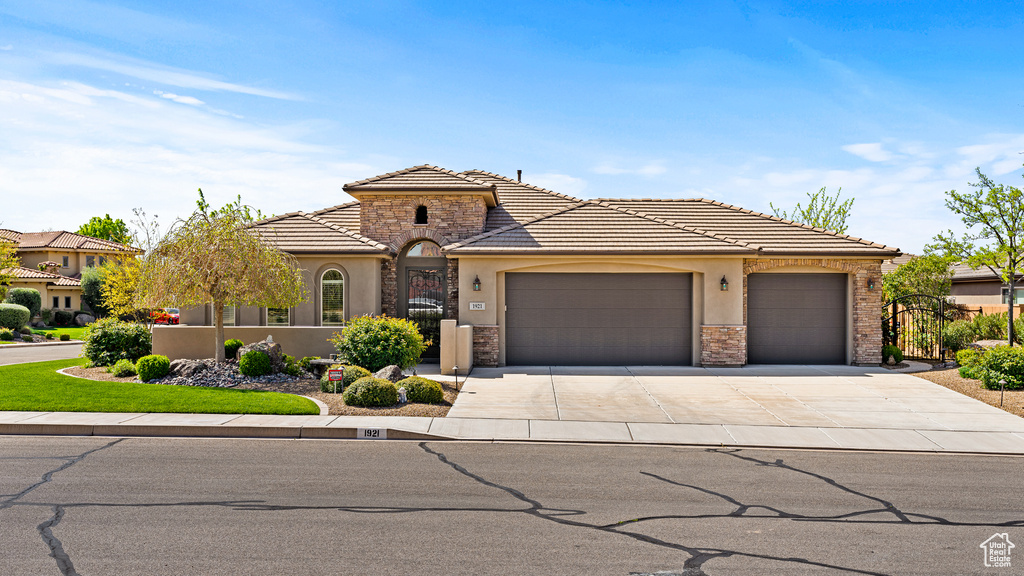 View of front of property featuring a garage, concrete driveway, stone siding, a tiled roof, and stucco siding