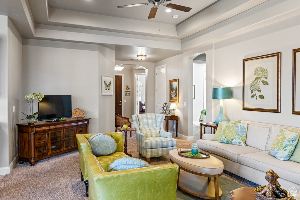 Living area with arched walkways, a raised ceiling, carpet flooring, and baseboards