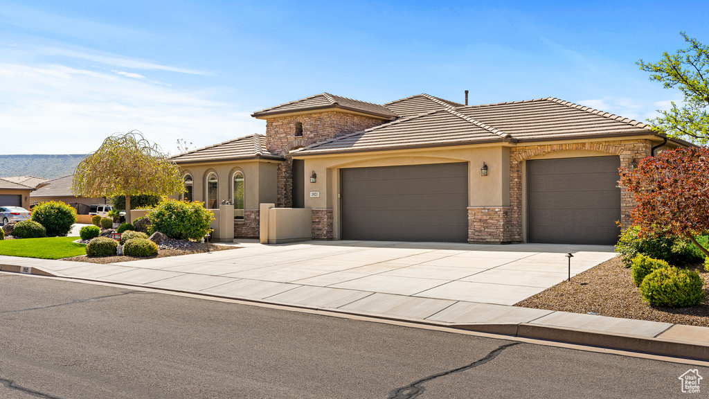 View of front facade with an attached garage, stone siding, driveway, and stucco siding