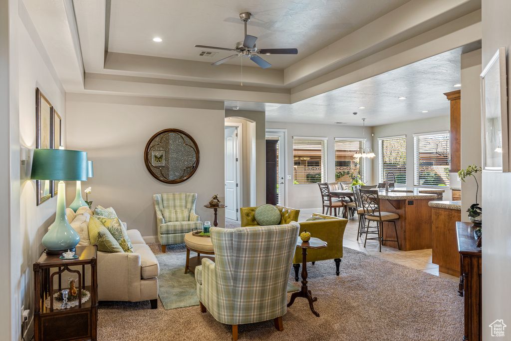 Living area featuring ceiling fan with notable chandelier, a tray ceiling, light carpet, and recessed lighting