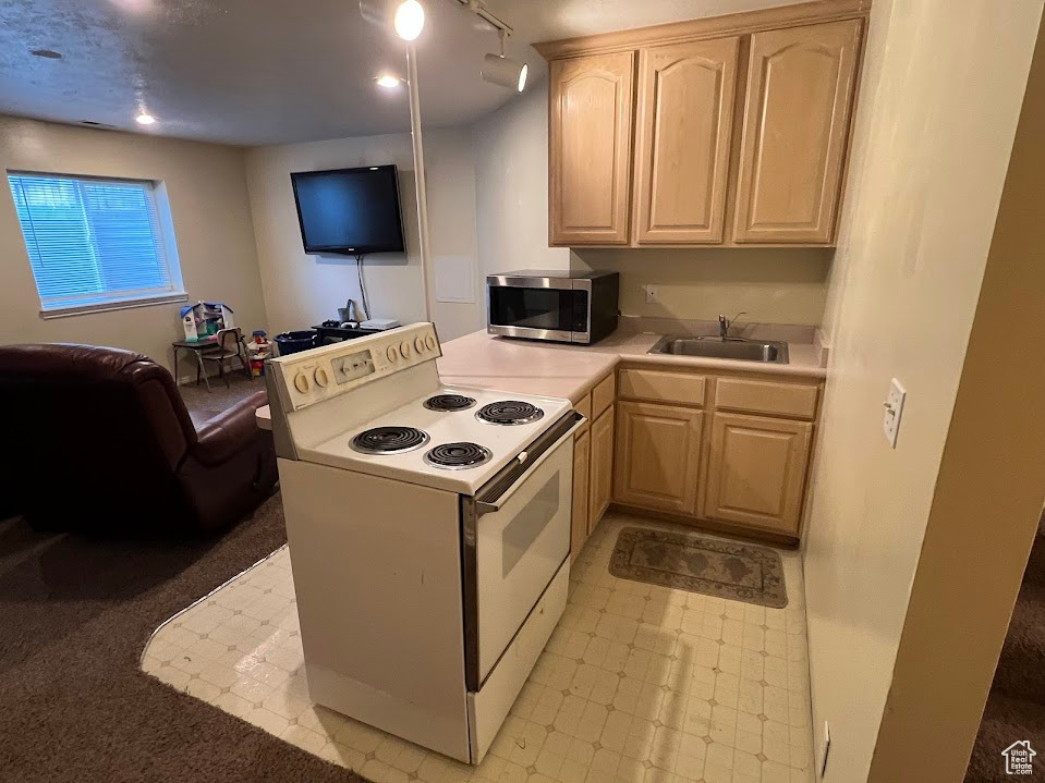 Kitchen with light brown cabinetry, a sink, stainless steel microwave, light countertops, and white range with electric stovetop