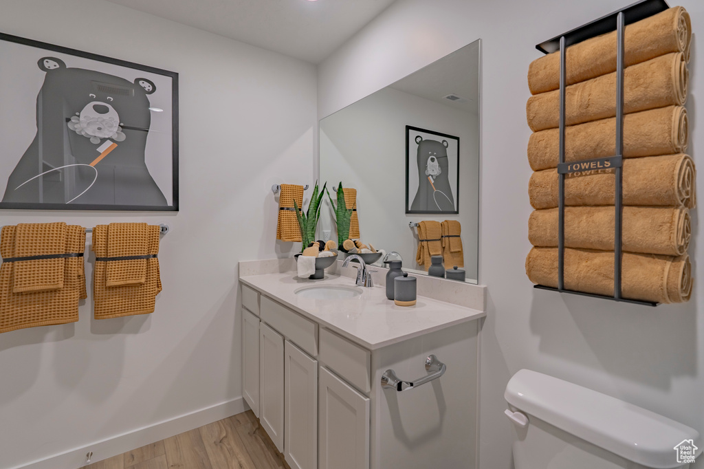 Half bathroom featuring toilet, baseboards, wood finished floors, and vanity