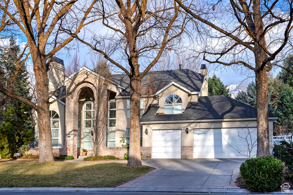 Traditional-style home featuring brick siding, a chimney, stucco siding, concrete driveway, and a garage