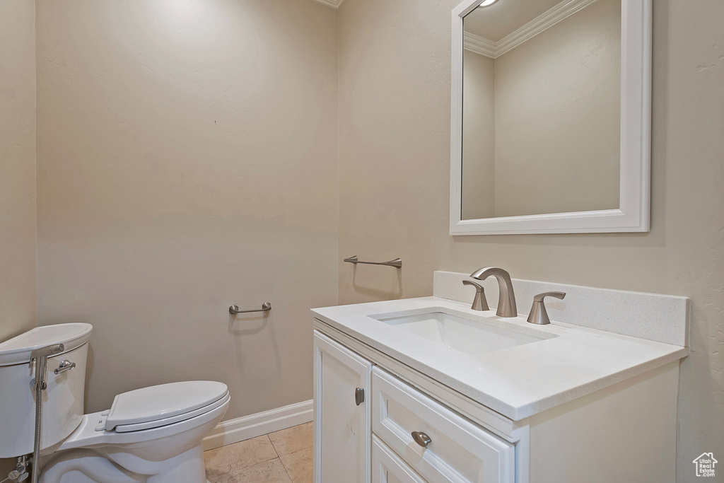 Half bath featuring toilet, vanity, baseboards, tile patterned floors, and crown molding