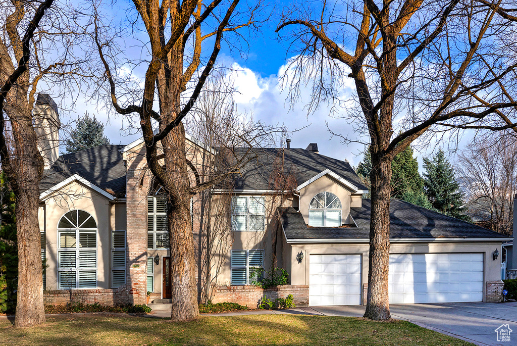 View of front of home featuring brick siding, a front yard, concrete driveway, and stucco siding