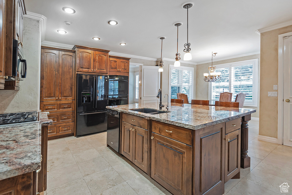 Kitchen featuring a sink, ornamental molding, light stone countertops, black appliances, and a center island with sink