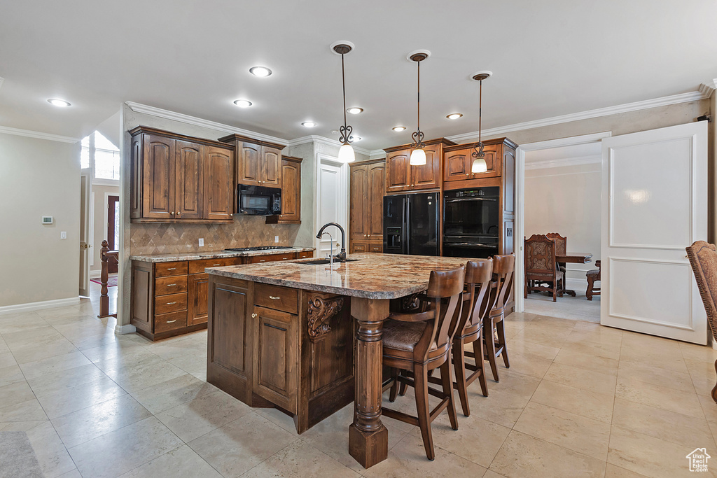 Kitchen with a breakfast bar, tasteful backsplash, a sink, an island with sink, and black appliances