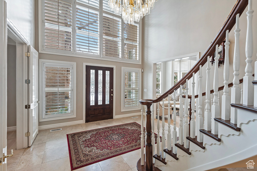 Tiled foyer featuring visible vents, stairway, a high ceiling, an inviting chandelier, and baseboards