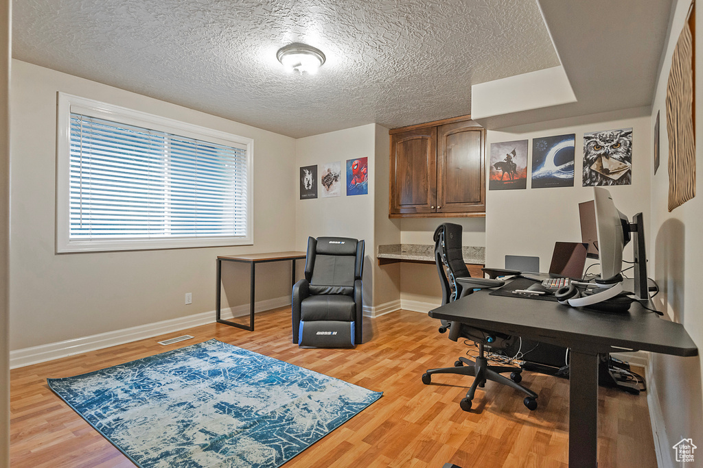 Office space featuring visible vents, baseboards, light wood-style flooring, a textured ceiling, and built in desk