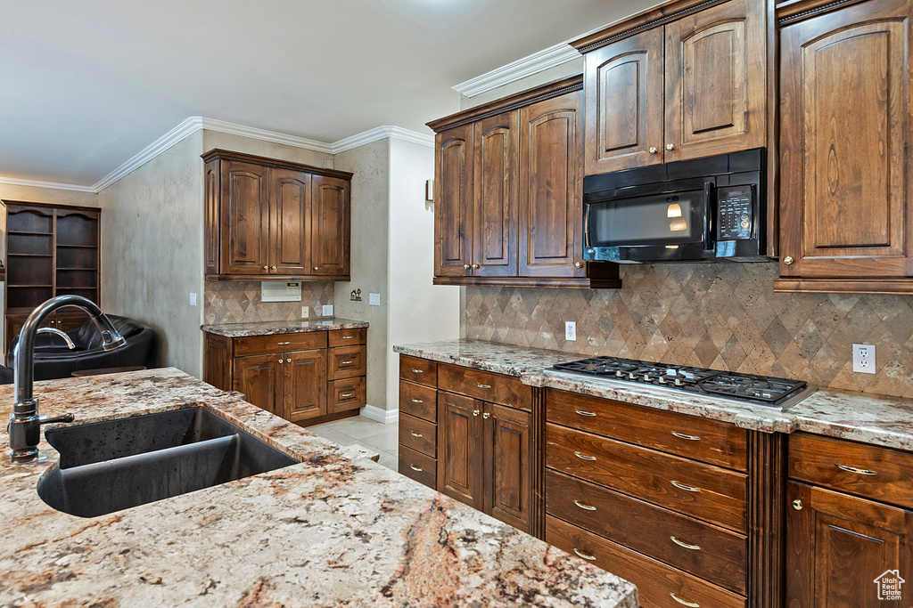 Kitchen featuring light stone counters, stainless steel gas cooktop, ornamental molding, a sink, and black microwave