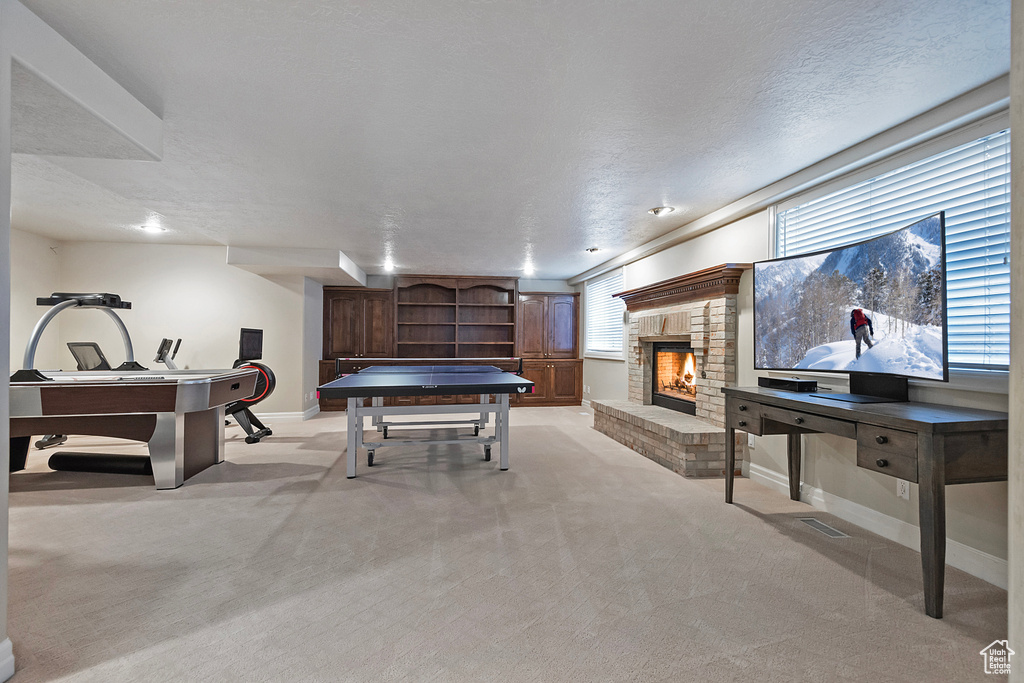 Playroom with a brick fireplace, baseboards, a textured ceiling, and light colored carpet