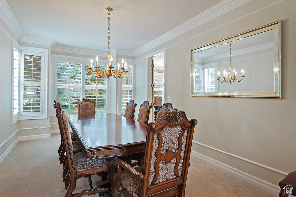 Carpeted dining space with baseboards, ornamental molding, and an inviting chandelier