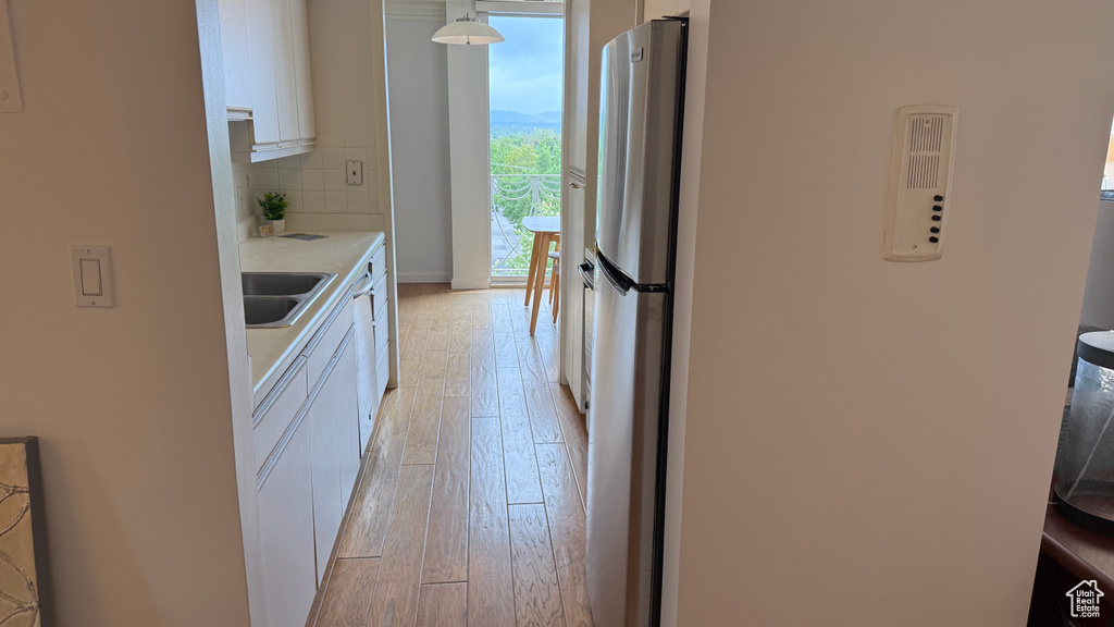 Kitchen featuring freestanding refrigerator, white cabinetry, light wood-style floors, light countertops, and decorative backsplash